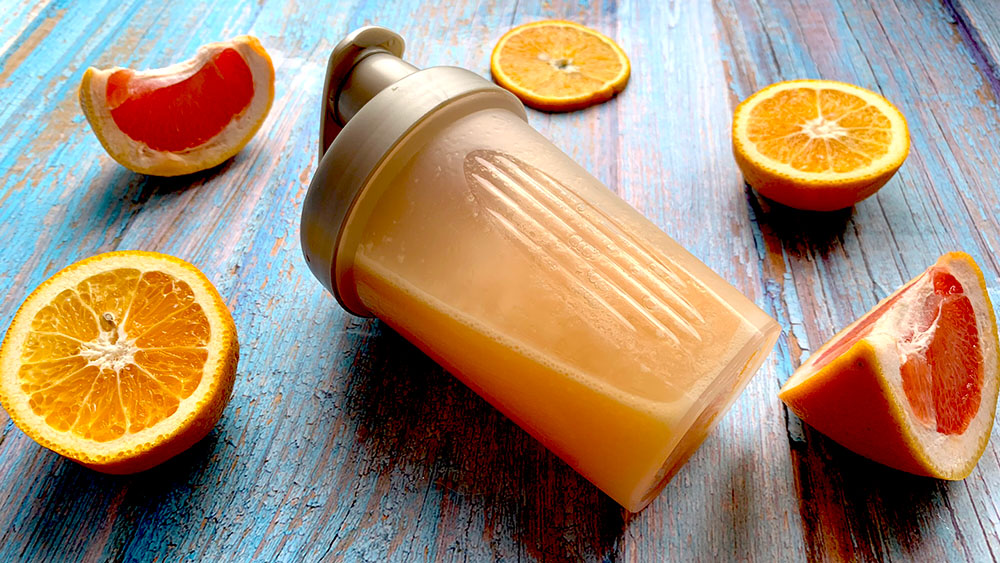 Iontový nápoj v športovom šejkry a rozkrojenými citrusmi na modrom drevenom podklade