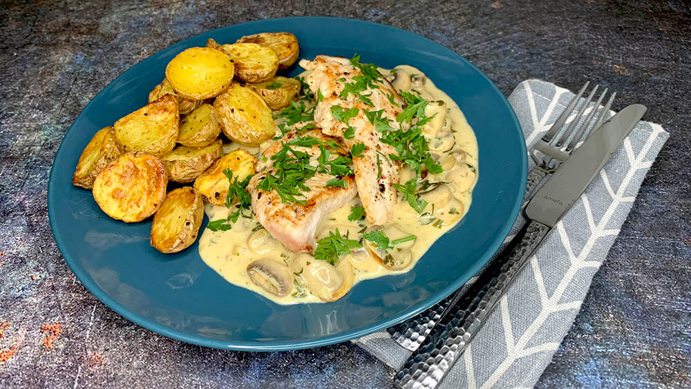 hubová omáčka s morčacím steakom a pečenými zemiakmi na modrom tanieri posypané čerstvou petržlenovou vňaťou