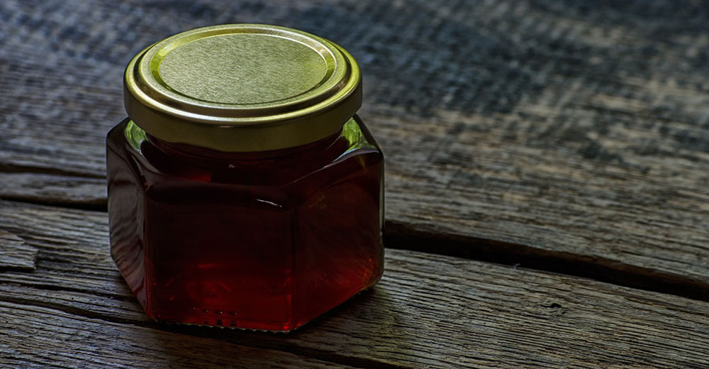 Tmavý med v zaváraninovom pohári na drevenom podklade